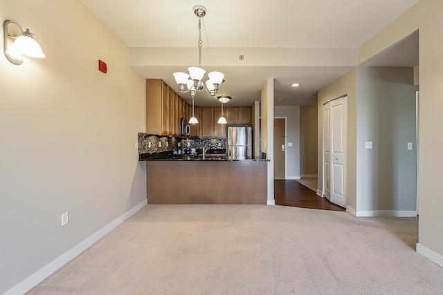 kitchen featuring dark countertops, dark carpet, freestanding refrigerator, tasteful backsplash, and a notable chandelier