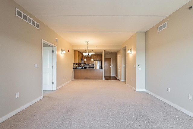 unfurnished room featuring visible vents, light colored carpet, and a notable chandelier