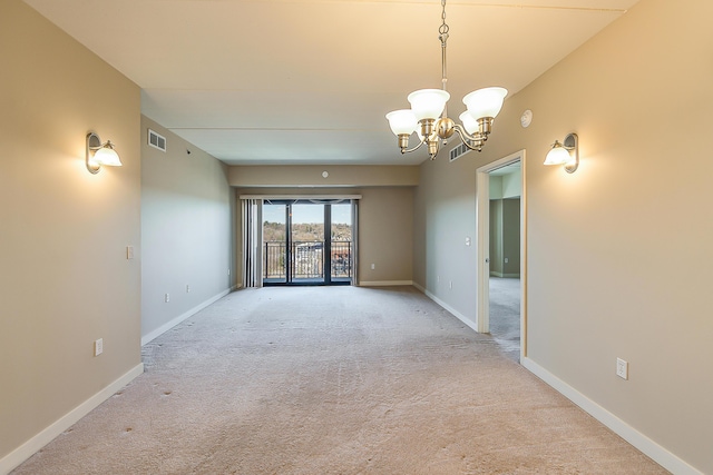 spare room featuring a notable chandelier, visible vents, baseboards, and light carpet