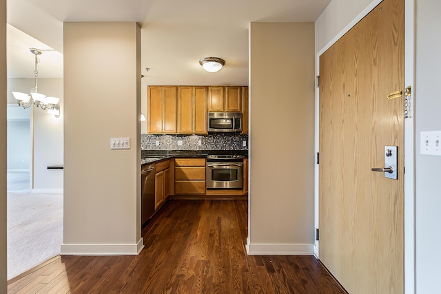 kitchen with dark countertops, decorative backsplash, a chandelier, stainless steel appliances, and dark wood-style floors