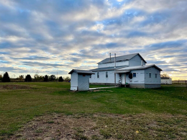rear view of property featuring a yard, a storage unit, metal roof, and an outbuilding