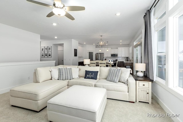 living area featuring light carpet, ceiling fan with notable chandelier, baseboards, and recessed lighting