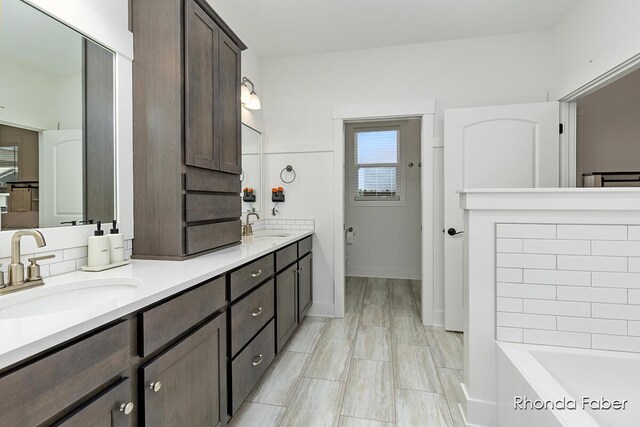 full bath featuring double vanity, a tub, baseboards, and a sink
