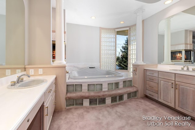 7635 Sandy Hollow Dr SE, Alto, MI 49302 - bathroom featuring decorative columns, two vanities, a bath, a glass covered fireplace, and recessed lighting