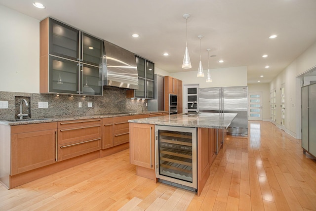 20 Hiawatha Dr, Battle Creek, MI 49015 - kitchen featuring wine cooler, wall chimney range hood, built in appliances, backsplash, and a kitchen island with sink