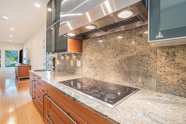 20 Hiawatha Dr, Battle Creek, MI 49015 - kitchen with wall chimney exhaust hood, brown cabinets, black electric stovetop, light stone counters, and backsplash