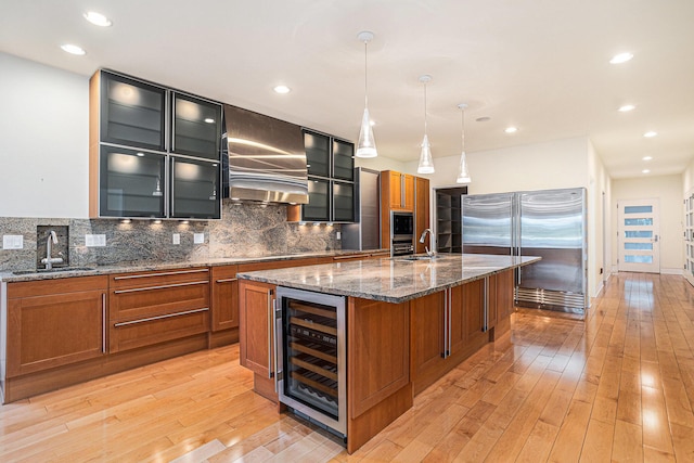 20 Hiawatha Dr, Battle Creek, MI 49015 - kitchen with built in refrigerator, beverage cooler, wall chimney exhaust hood, brown cabinetry, and tasteful backsplash