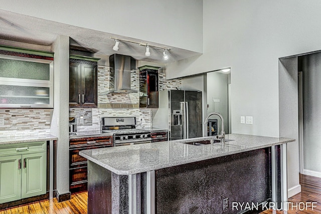 kitchen featuring wall chimney exhaust hood, stainless steel appliances, a sink, backsplash, and light stone counters