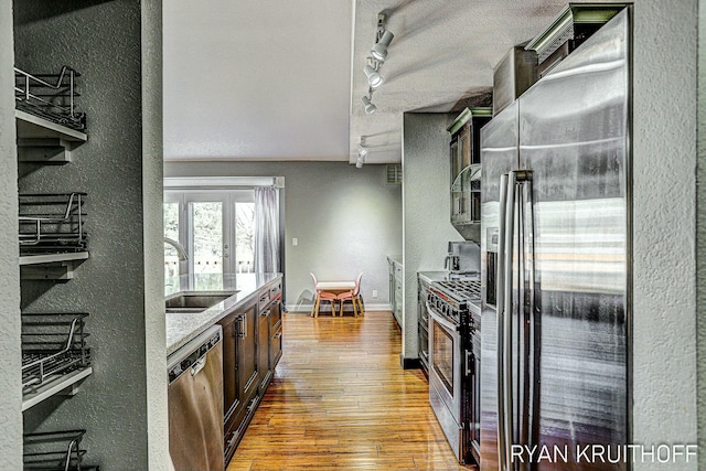 kitchen featuring stainless steel appliances, track lighting, wood finished floors, a textured wall, and a sink