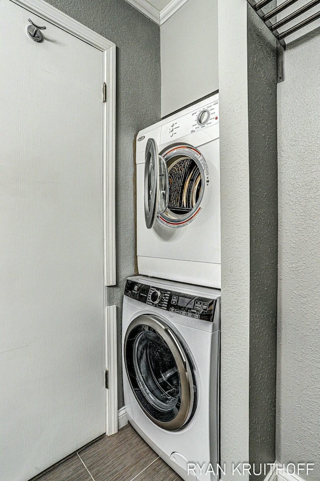 clothes washing area featuring a textured wall, stacked washing maching and dryer, laundry area, and crown molding
