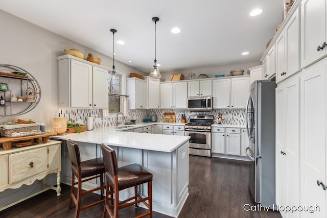 kitchen featuring a peninsula, a sink, decorative backsplash, a breakfast bar, and appliances with stainless steel finishes