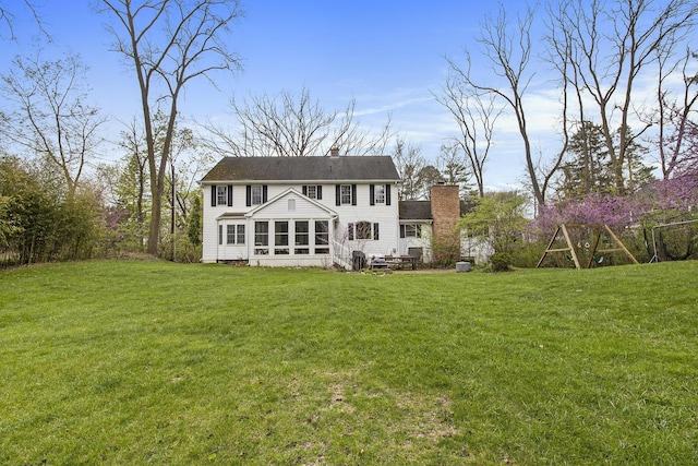 rear view of property with a sunroom, a yard, and a chimney