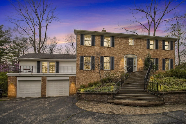 colonial home with a chimney, an attached garage, driveway, and brick siding