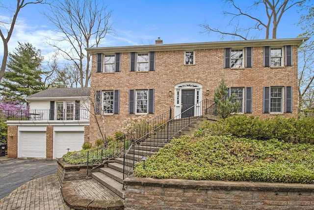 colonial home featuring brick siding, driveway, a chimney, and a garage