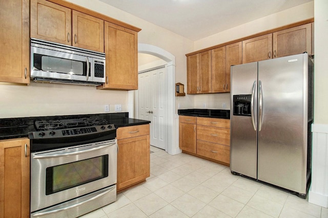 8 Georgia Ct, Pentwater, MI 49449 - kitchen with light tile patterned flooring, dark countertops, brown cabinets, arched walkways, and appliances with stainless steel finishes