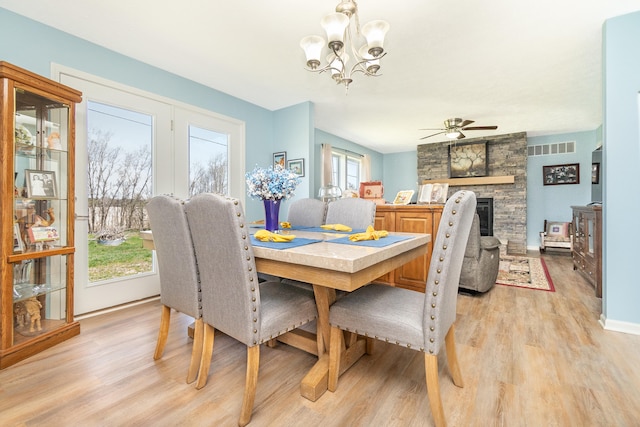 48320 Martz Rd, Van Buren Twp, MI 48111 - dining area with light wood-type flooring, baseboards, visible vents, ceiling fan with notable chandelier, and a stone fireplace