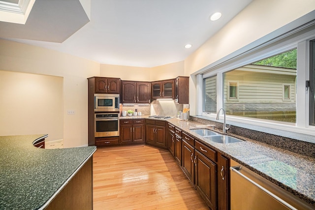 2925 Exmoor Rd, Ann Arbor, MI 48104 - kitchen featuring appliances with stainless steel finishes, a sink, light wood-style floors, dark stone countertops, and backsplash