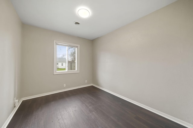 empty room with dark wood-style flooring, baseboards, and visible vents