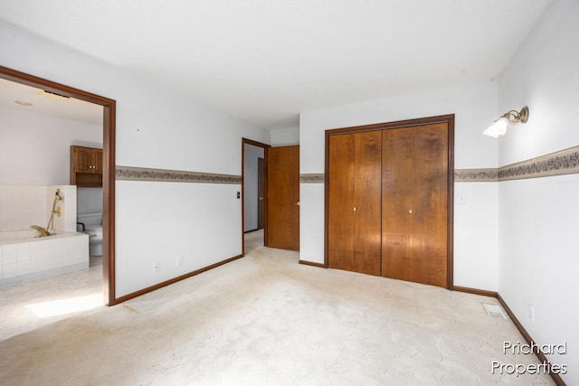 unfurnished bedroom featuring visible vents, a closet, baseboards, light colored carpet, and ensuite bathroom