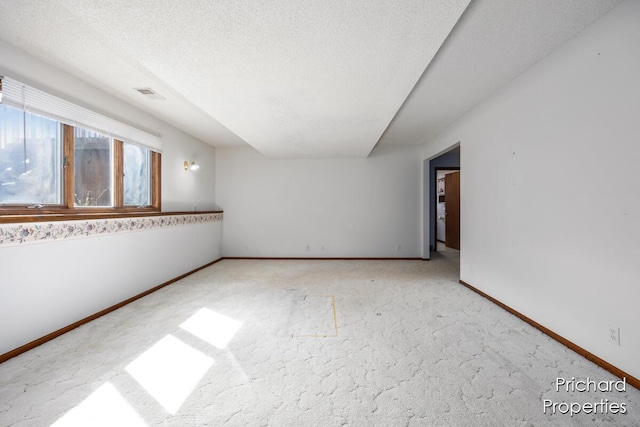 spare room with a textured ceiling, visible vents, carpet flooring, and baseboards