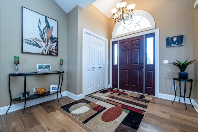 foyer featuring baseboards, wood finished floors, an inviting chandelier, and vaulted ceiling