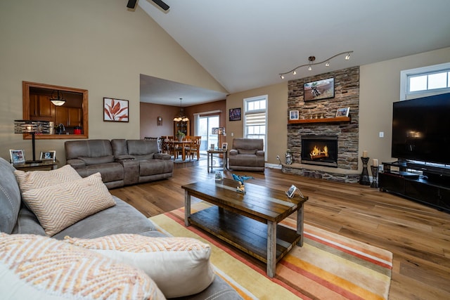 living area featuring a wealth of natural light, wood finished floors, high vaulted ceiling, and a stone fireplace