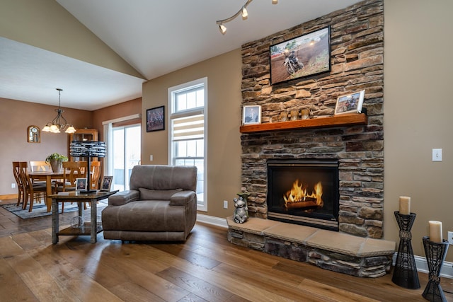 living room featuring vaulted ceiling, a notable chandelier, a stone fireplace, and baseboards