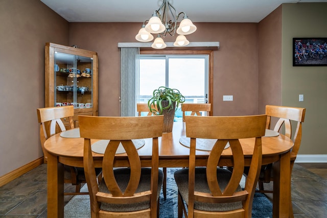 dining area with an inviting chandelier, stone finish floor, and baseboards