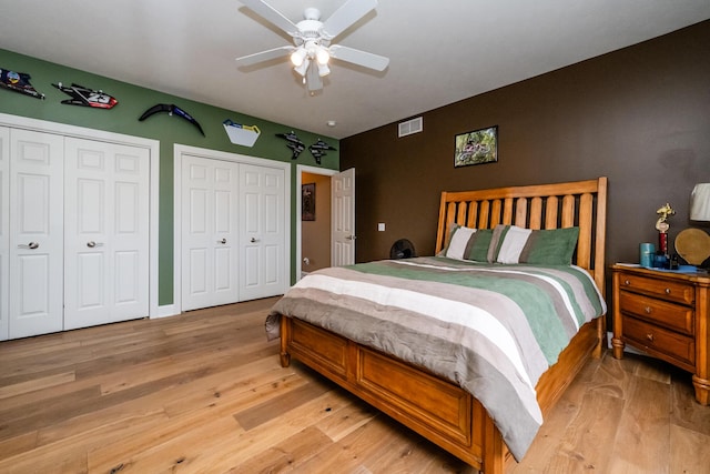 bedroom featuring multiple closets, visible vents, ceiling fan, and light wood finished floors