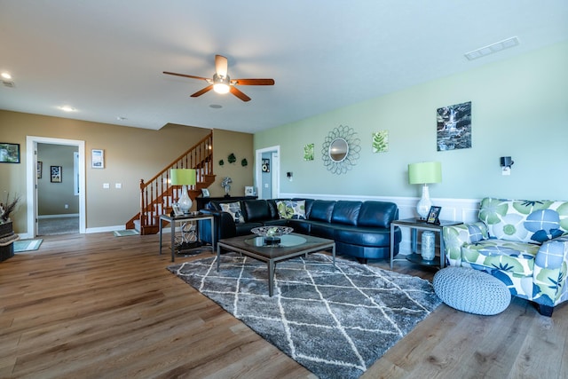living area with stairway, visible vents, a wainscoted wall, wood finished floors, and a ceiling fan