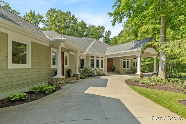 17180 Shore Oaks W Ln, Holland, MI 49424 - back of property with a chimney, concrete driveway, a shingled roof, and covered porch