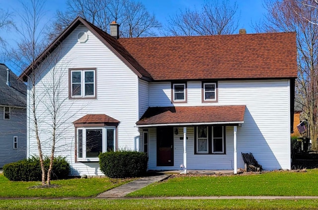 traditional-style home featuring a chimney, a porch, a front lawn, and roof with shingles