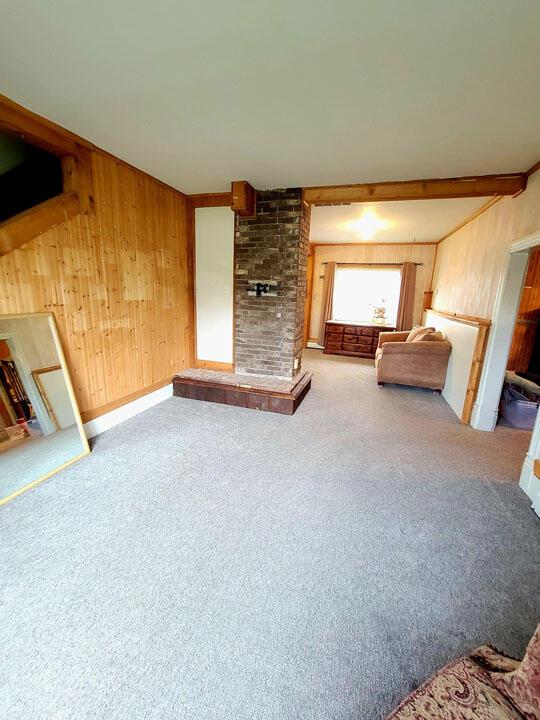 unfurnished living room featuring wooden walls, a brick fireplace, and carpet flooring