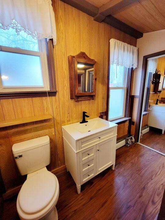 bathroom featuring wood finished floors, a healthy amount of sunlight, toilet, and beamed ceiling