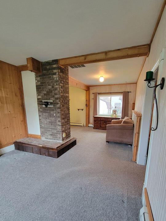 living room featuring visible vents, beamed ceiling, a baseboard heating unit, and wooden walls