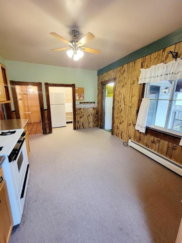 unfurnished bedroom with a ceiling fan, wood walls, carpet, freestanding refrigerator, and a baseboard radiator