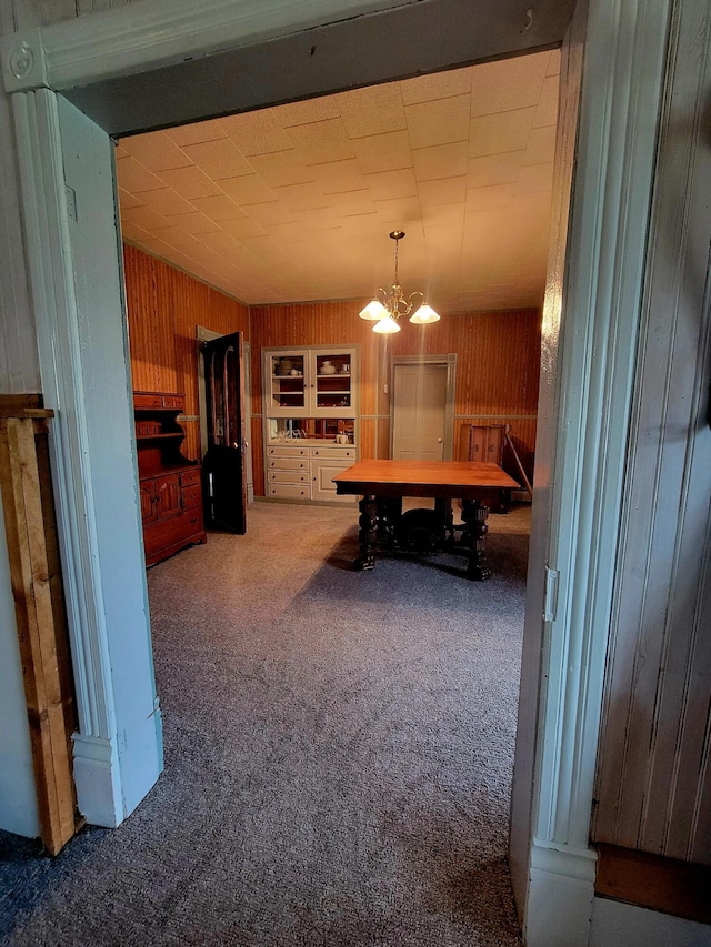 dining space with wooden walls, a notable chandelier, and carpet floors