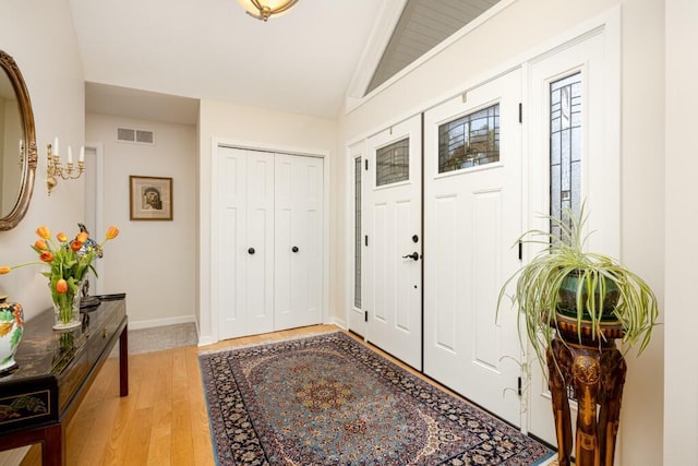 entrance foyer with baseboards, lofted ceiling, visible vents, and light wood-style flooring