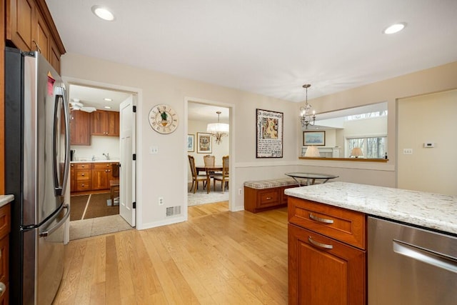 kitchen with light wood finished floors, stainless steel appliances, an inviting chandelier, visible vents, and brown cabinetry