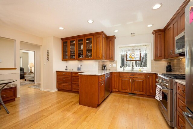 kitchen featuring light wood-style flooring, decorative backsplash, brown cabinetry, and stainless steel appliances