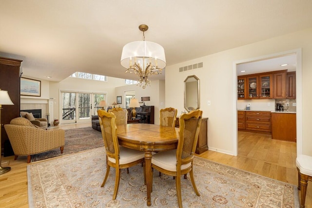 dining space featuring a tiled fireplace, a notable chandelier, visible vents, and light wood-type flooring