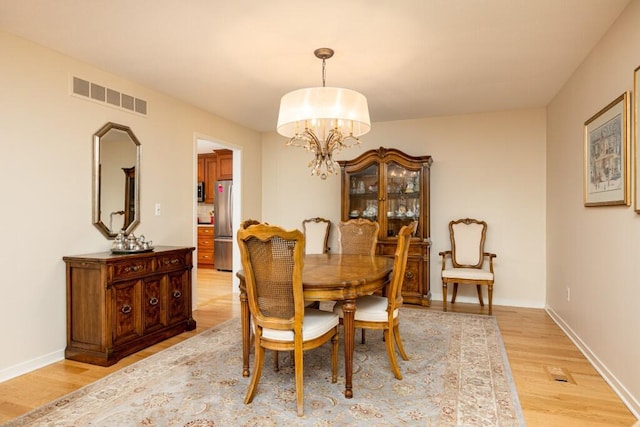 dining space with baseboards, light wood-style flooring, visible vents, and a notable chandelier