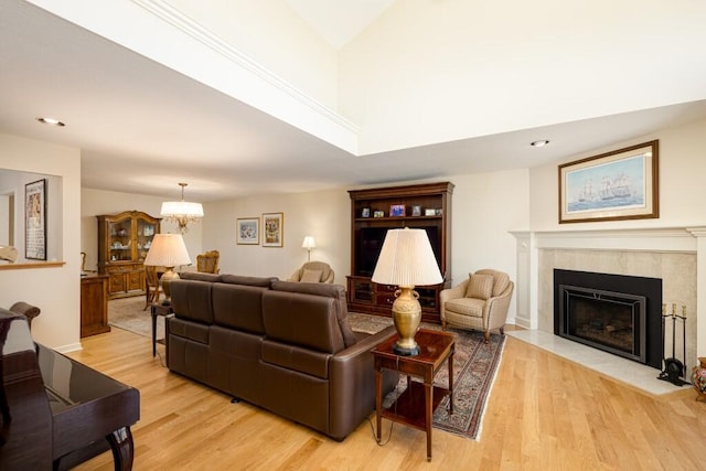 living room with recessed lighting, a high end fireplace, an inviting chandelier, and light wood-style flooring