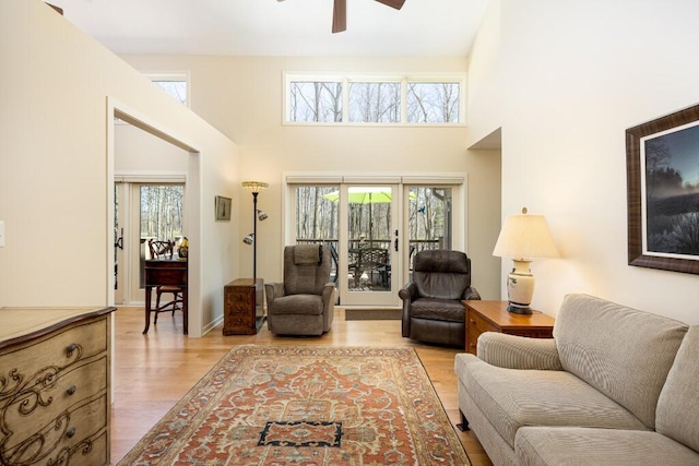 living area featuring light wood-type flooring, a high ceiling, ceiling fan, and a healthy amount of sunlight