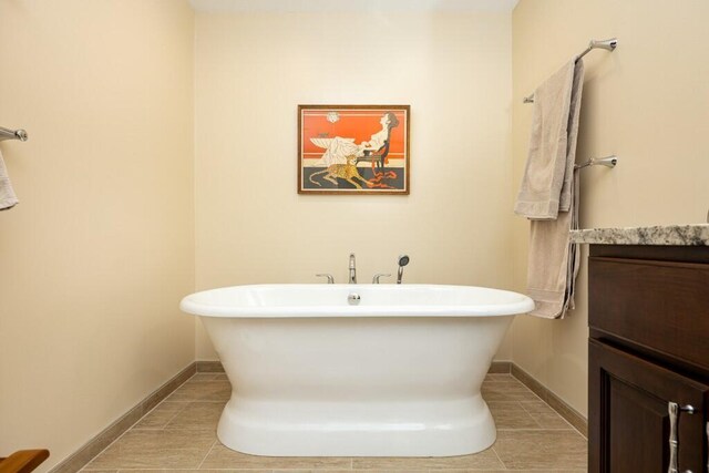 bathroom with baseboards, a soaking tub, tile patterned floors, and vanity