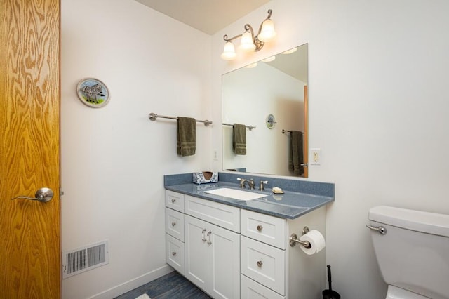 bathroom featuring toilet, vanity, visible vents, and baseboards