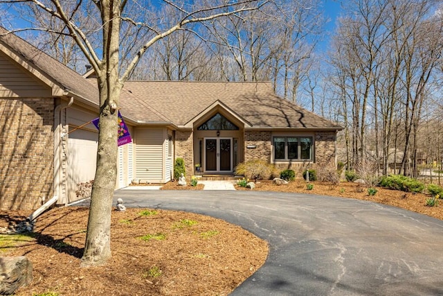 single story home featuring brick siding, driveway, a shingled roof, and a garage