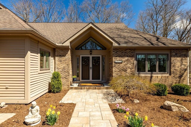 view of exterior entry with french doors, brick siding, and roof with shingles