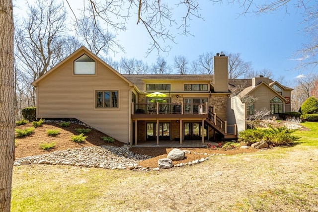 back of house with a chimney, a deck, stairs, and a lawn