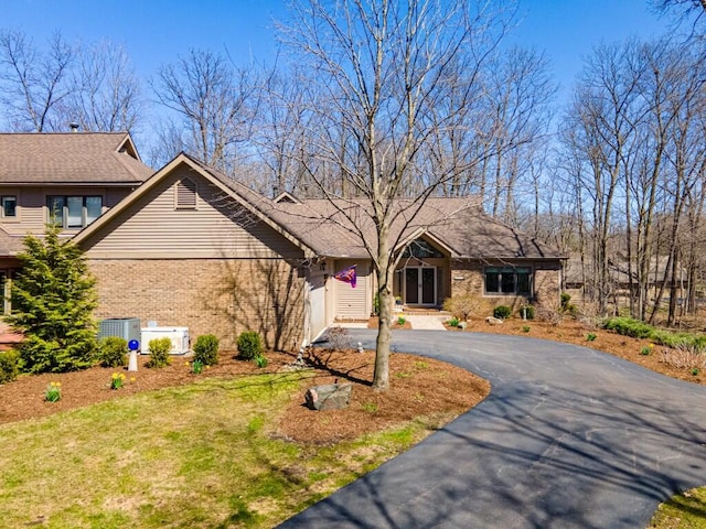 view of front of home with brick siding, an attached garage, driveway, and central air condition unit